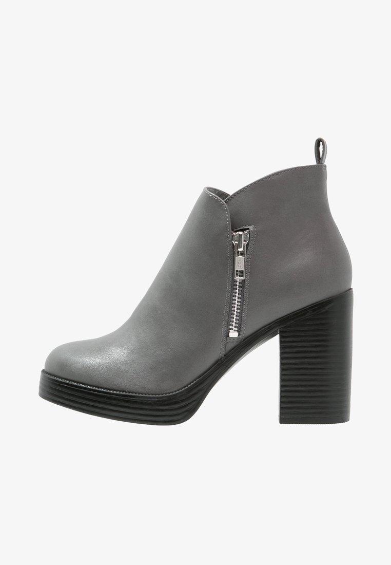 Bottine en cuir gris avec fermeture éclair latérale, talon haut épais noir superposé et languette à l'arrière.