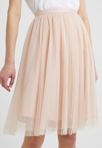 Gonna in tulle rosa chiaro con vita aderente, decorata con delicati motivi a pois, indossata da una persona con un top bianco.