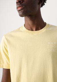 Round-neck yellow cotton t-shirt featuring a subtle printed logo on the chest, with short sleeves and a soft texture.