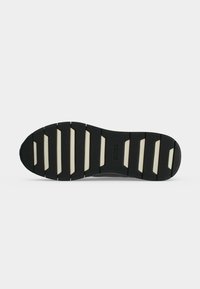 Semelle de chaussure noire avec des grips rectangulaires blancs et le logo "BOSS" embossé au centre, photographiée sur un fond blanc uni.