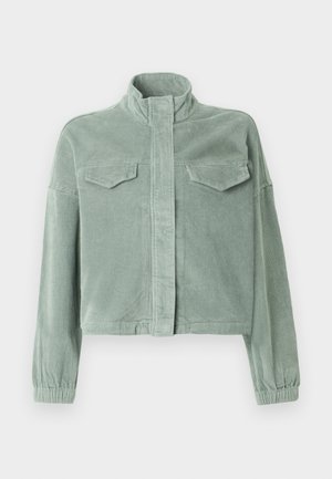 Mentazöld kordbársony dzseki magas gallérral, elöl cipzárral és két mellzsebbel. Rugalmas mandzsettákkal és enyhén rövidített fazonnal rendelkezik.