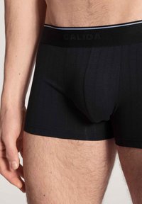 Zwarte boxershorts van fijn geribbeld materiaal, zachte stof en een elastische tailleband met een subtiel logo en contrasterende streepdetails.