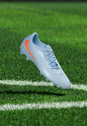 Chaussure de football Nike bleu clair avec un swoosh orange flottant au-dessus d'un terrain d'herbe verte avec des lignes blanches.