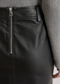 Zwarte leren rok met een zilveren rits aan de achterkant, aansluitend ontwerp, soepele textuur en een tailleband met riemlussen.