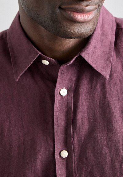 Cămașă din in burgund cu guler tip button-down, având butoane albe și un finisaj ușor texturat. Vedere apropiată care evidențiază detalii.