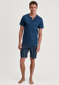 Marineblauw korte mouwen henley shirt met een knoopsluiting, gecombineerd met gestreepte shorts in marineblauw en perziktinten.