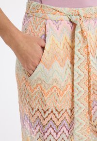 Spitzenrock in Pastellfarben mit Zickzackmuster. Ausgestattet mit einem gebundenen Bund und seitlichen Taschen. Leichte, transparente Textur.