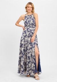 Løs, marineblå maxi kjole med blomsterprint, høj slidser og halterneck-design. Har cremefarvede blomster mønstre og et blødt, let stof.