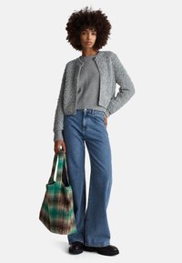 Szary, puszysty, krótki kardigan noszony na szarym swetrze, zestawiony z szerokimi niebieskimi dżinsami i wzorzystą zieloną torbą na ramię. Całość uzupełniają czarne buty.