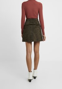 Gonna a stampa leopardata con forma svasata, abbinata a un top aderente a maniche lunghe color ruggine. Stivaletti bianchi alla caviglia completano l'outfit.