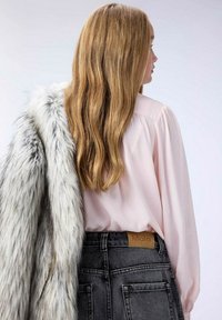 Grå fuskpälsjacka draperad över en ljusrosa blus, tillsammans med grå denimshorts med hög midja och en texturerad midjebandsetikett.