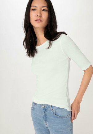 Lichtgroen, getailleerd T-shirt met korte mouwen, zachte textuur, ronde halslijn en zijnaad. Gepaard met lichtblauwe jeans.