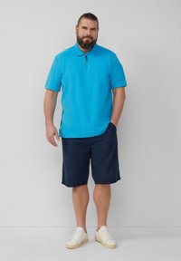 Turkusowa koszulka polo z krótkim rękawem i zapięciem na zamek, w połączeniu z granatowymi szortami i białymi trampkami. Gładki fason, bawełniany materiał.