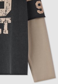 Primo piano di una camicia a maniche lunghe nera e beige con testo stampato usurato e il numero 9 sulla manica.