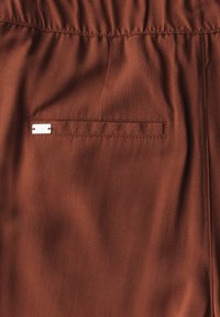 Bruin stof met een gladde textuur, voorzien van een platte zak en een klein merklabel met de tekst "Street One Studio."