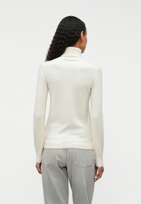 Cream-colored turtleneck sweater made from soft, lightweight material, featuring long sleeves and ribbed cuffs, worn over gray jeans.