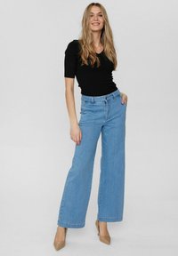 Jeans bleu clair à jambes larges avec une taille haute et un design classique à cinq poches, associés à un haut noir à côtes ajusté.