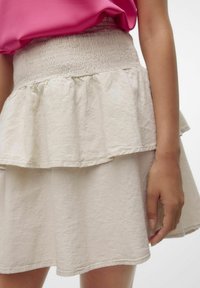 Gonna a strati beige chiaro con una finitura texture. Presenta una vita arricciata e un design a strati, con una silhouette svasata.