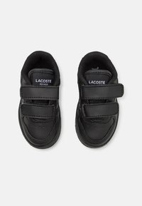 Mustad musträdid, millel on kaks takjakinnitust, pehmendatud kaelus ja tekstuuriga detailid varvaste juures. Lacoste bränding kee peal.