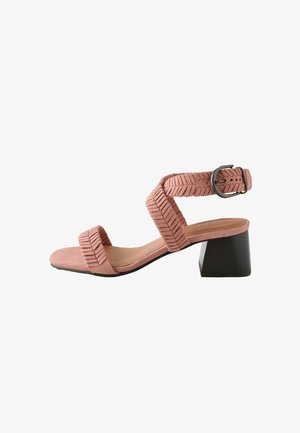 Sandale en daim rose avec des brides texturées, boucle à la cheville et talon bloc noir, présentée sur fond blanc.