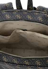 Plecak z ciemnoniebieskiego syntetycznego materiału z wzorem złotego logo. Wnętrze jest beżowe i wykonane z tkaniny z powtarzającym się brandingiem.