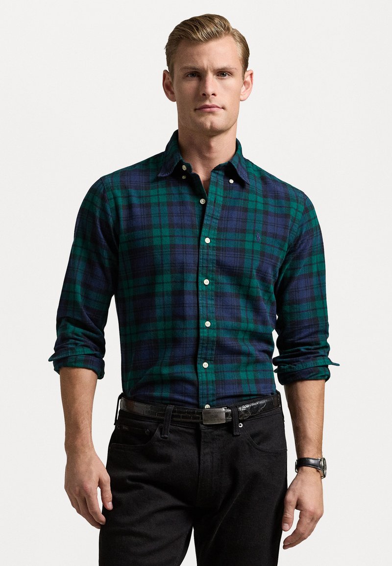 Geruite shirt in donker groen en marineblauwe flanellen stof, met een knoopsluiting, lange mouwen, witte knopen, gedragen met een zwarte spijkerbroek en een riem.