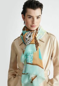 Écharpe multicolore avec des imprimés animaliers et des motifs géométriques. Fabriquée en tissu doux, avec des bords frangés. Portée de manière décontractée autour du cou.