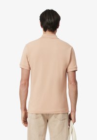 Polo de manga corta en tela de algodón color durazno claro. Presenta un collar clásico y una superficie ligeramente texturizada. Corte casual y dobladillo limpio.