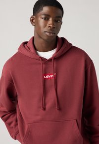Bordo dukserica s kapuljačom izrađena od mekog materijala, s prednjim džepom, kapuljačom na vezanje i crvenim Levi's logotipom na prsima.