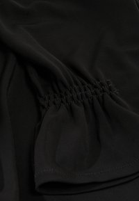 Tela negra con una textura suave, que presenta costuras fruncidas. El diseño muestra un suave drapeado y un sutil brillo.