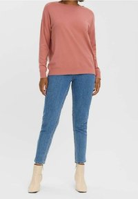 Rosa Langarmpullover kombiniert mit blauen geraden Jeans und cremefarbenen Stiefeletten. Der Pullover hat eine lockere Passform und gerippte Bündchen.