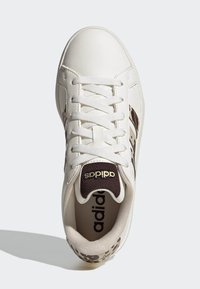 Bijela kožna tenisica s teksturiranim smeđim detaljima, vezicama i Adidas logotipom. Leopardski uzorak na peti i unutarnjem oblogu.