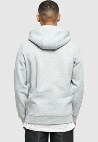 Hanorac gri cu o glugă mare, căptușită, manșete și tiv cu elastic. Textură moale și croială lejeră. Fără logo-uri sau modele vizibile.