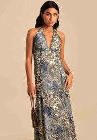 Vestido maxi con cuello halter, estampado de paisley en azul y verde sobre un fondo claro, con una silueta fluida y un brillo sutil.