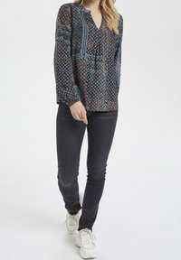 Długa bluzka z długim rękawem w ciemnoniebieskim kolorze z wielokolorowymi akcentami, z dekoltem w kształcie litery V i zebranymi mankietami, w połączeniu z ciemnymi dżinsami i białymi trampkami.