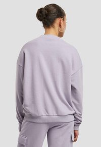 Felpa lilla con vestibilità rilassata, polsini e orlo ribattuti. Tessuto morbido con spalle scese e design semplice.