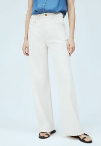 Korkeavyötäröiset, leveät farkut off-white-denimistä, joissa on etutaskut ja napitus. Yhdistetty mustien litteiden sandaalien kanssa.