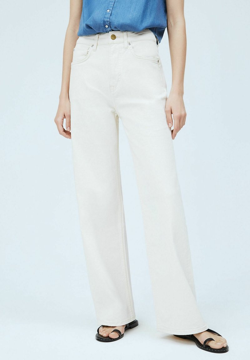 Korkeavyötäröiset, leveät farkut off-white-denimistä, joissa on etutaskut ja napitus. Yhdistetty mustien litteiden sandaalien kanssa.