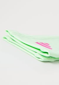 Groene rekbare stof scrunchies gestapeld, met een gladde textuur en een levendig roze logo detail aan de ene kant.