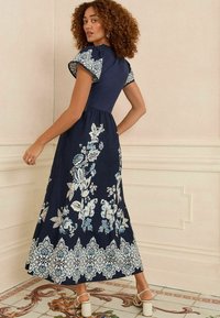 Abito maxi blu navy con ricami floreali bianchi e blu, maniche a sbuffo corte e gonna svasata. Il motivo elegante sull'orlo aggiunge un tocco di dettagli.