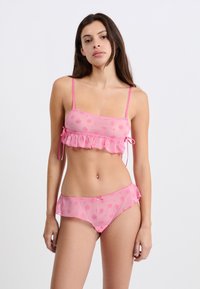 Ensemble de lingerie rose comprenant un crop top à volants avec des motifs floraux et des bretelles réglables, associé à une culotte hipster assortie.
