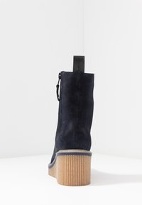 Botín de ante azul marino con tacón de goma texturizada, cremallera lateral y tira negra en la parte trasera. Acabado liso, con un diseño minimalista.
