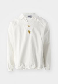 Bílý svetr s límečkem, zdobený zlatě vyšitými logy, včetně lva a trefoil Adidas, texturovaná látka a elastické manžety.