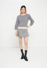 Strickpullover in Marineblau und Creme, mit einem gemusterte Design und ausgestellten Ärmeln. Kombiniert mit einem hellgrauen, ausgestellten Rock und schwarzen Schuhen.
