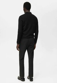 Schwarzer Pullover mit slim fit, kombiniert mit dunklen Hosen. Glatte Textur, minimalistisch design und saubere Nähte. Schwarze Schuhe runden das Erscheinungsbild ab.