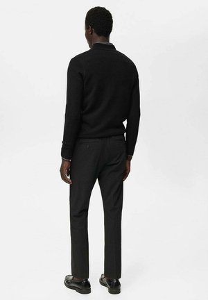 Črna pulover s slim fit krojem, kombiniran s temnimi hlačami. Gladka tekstura, minimalističen dizajn in urejene šivane podrobnosti. Črne čevlje dopolnjujejo videz.
