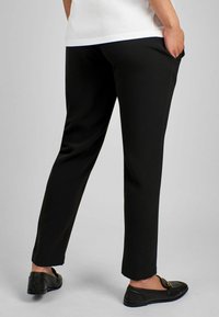 Pantaloni neri su misura con design a gamba dritta. Realizzati in tessuto liscio, con tasche laterali e indossati con mocassini neri.