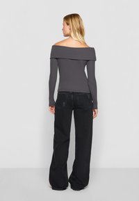 Szara bluzka z długim rękawem z odkrytymi ramionami o prążkowanej fakturze, w zestawieniu z czarnymi spodniami typu wide-leg. Minimalistyczny design, odpowiednia do codziennego użytku.