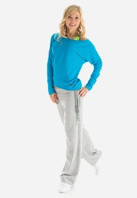 Light blue off-shoulder sweatshirt and gray sweatpants with colorful drawstring accents. Model wears white sneakers and a green top underneath.