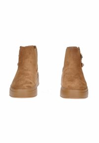 Stivali ankle in suede marrone con finitura liscia, pannelli laterali elastici e suole in gomma. Presentano un dettaglio decorativo con zip sul lato esterno.